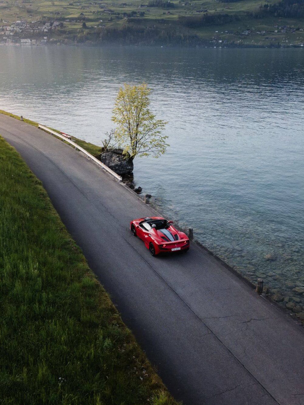 Ferrari driving along a scenic road beside a Swiss lake.