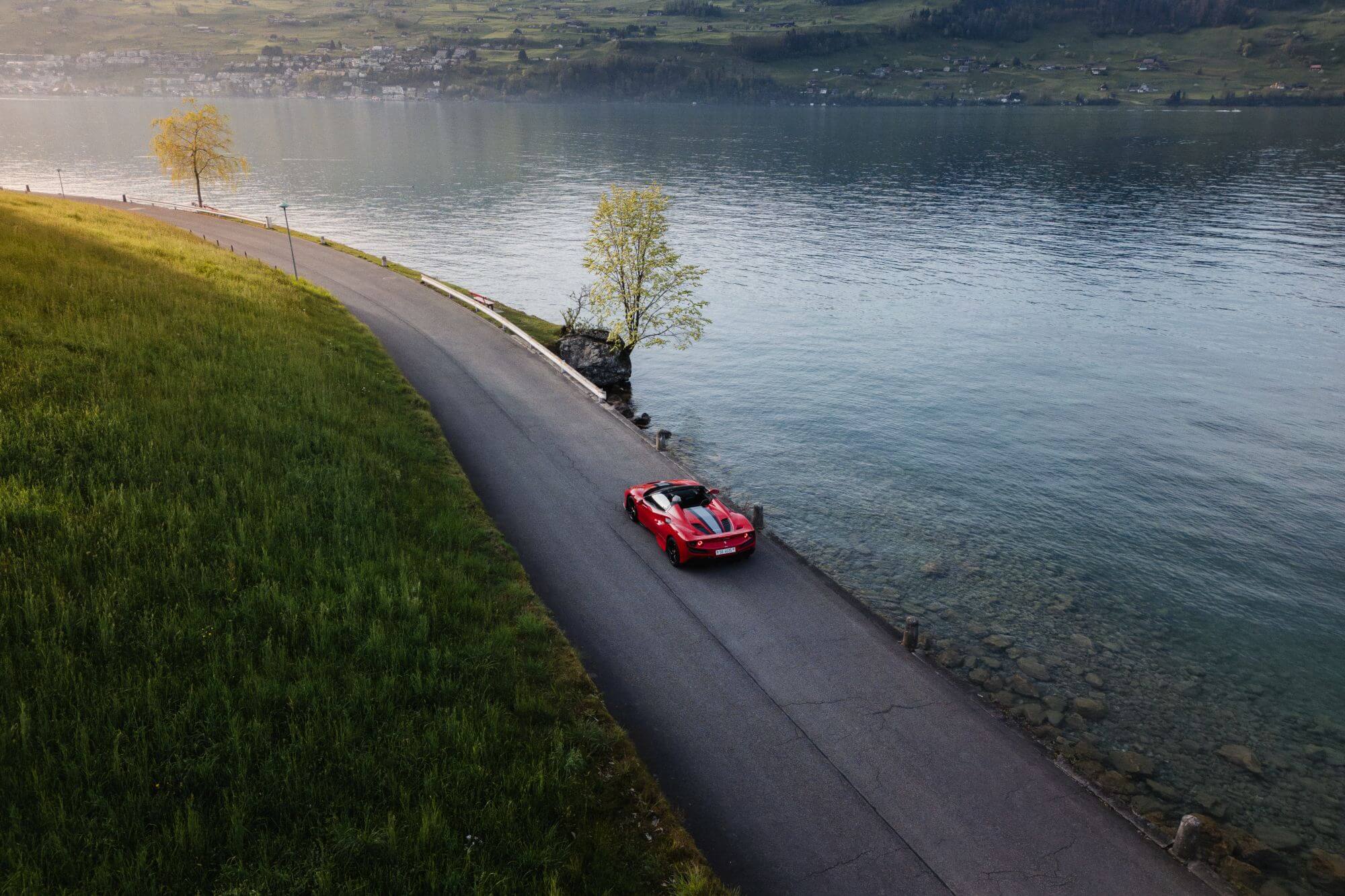 Ferrari driving along a scenic road beside a Swiss lake.