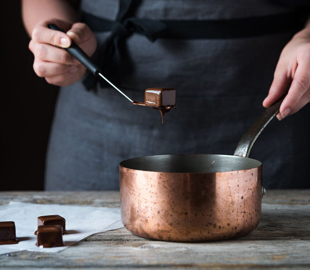 Participant dipping a chocolate truffle into a saucepan filled with melted chocolate during a Swiss chocolate workshop
