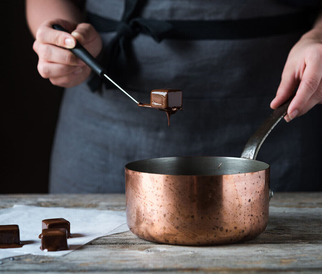 Participant dipping a chocolate truffle into a saucepan filled with melted chocolate during a Swiss chocolate workshop